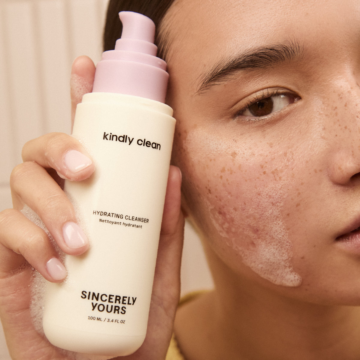 100 ml | 30 ml | Person holding a 'kindly clean' hydrating cleanser bottle close to their face.