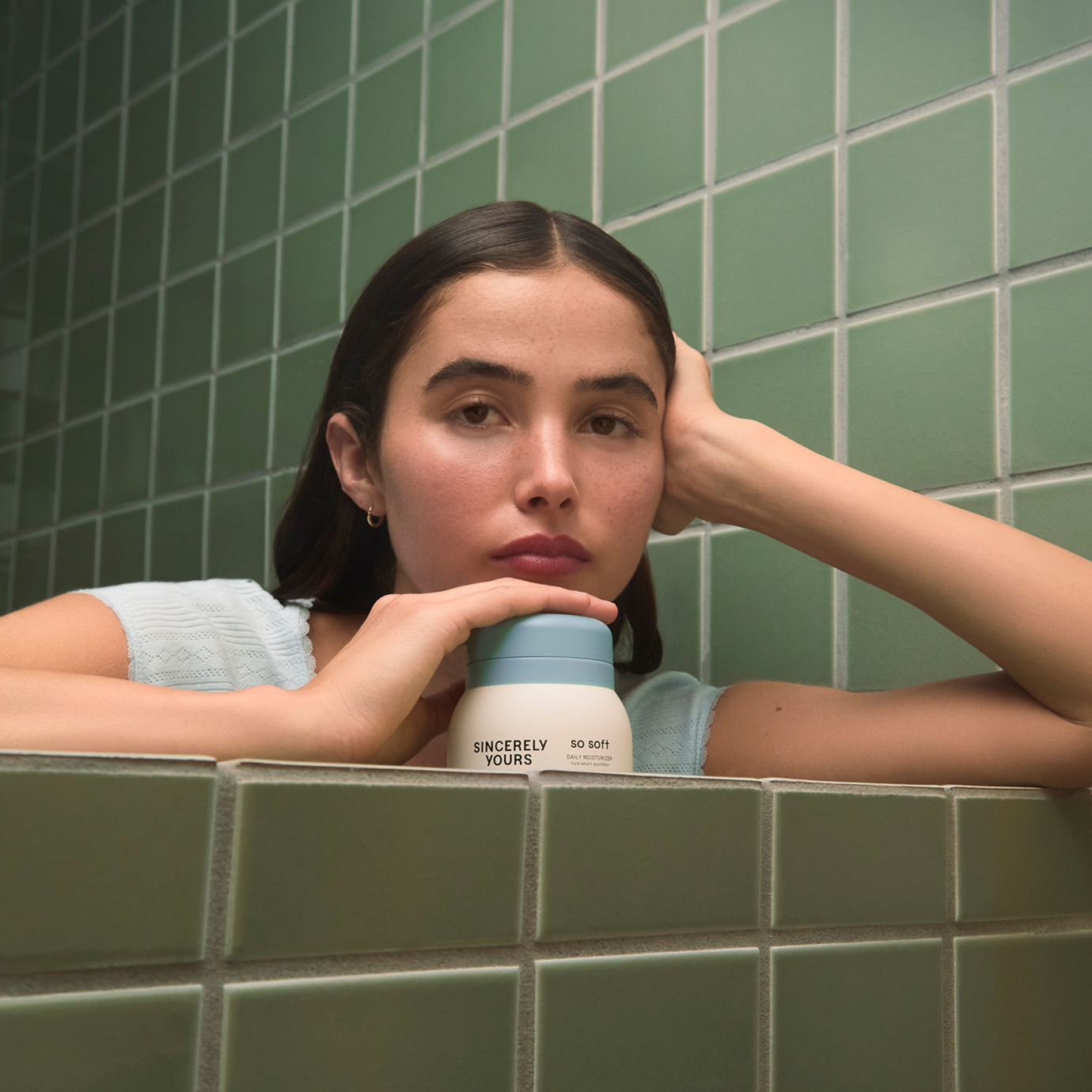 Woman holding a cylindrical product labeled 'Sincerely Yours' against a green tiled wall.