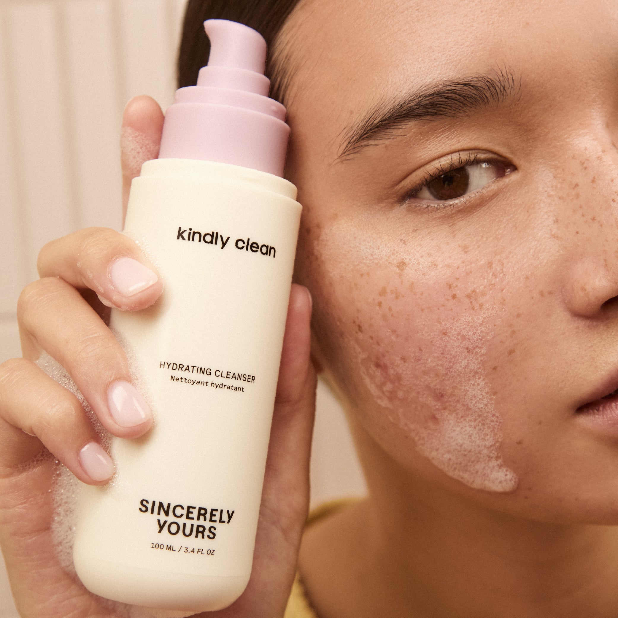 Person holding a 'kindly clean' hydrating cleanser bottle close to their face.