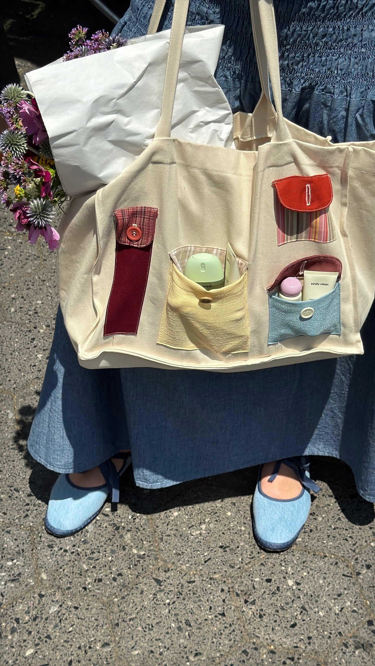 Beige tote bag with small compartments and colorful items, worn by a person on a street.